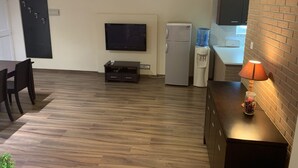 A modern living room with a flat-screen TV, a refrigerator, and a dining area with a table and chairs. - Less than five minutes from the beach, restaurants, supermarkets, bakery's (Paralimni)