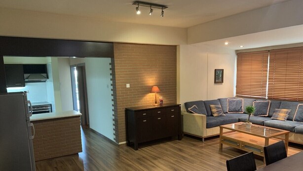 A modern living room with a sofa, coffee table, and a dining area. There is a kitchen visible in the background. - Less than five minutes from the beach, restaurants, supermarkets, bakery's (Paralimni)