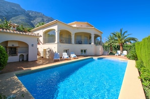A large swimming pool with white lounge chairs and a two-story building with arched windows and balconies.
