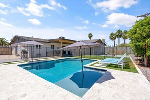 A swimming pool with a tiled deck, umbrellas, and lounge chairs.