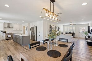 A spacious kitchen with modern appliances, a dining area with a wooden table and chairs, and a living room with a sofa and television.