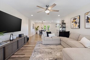 A modern living room with a flat-screen TV, a ceiling fan, and a dining area in the background. - 4BR + Casita w/ Pool + Outdoor Big Screen (Scottsdale)