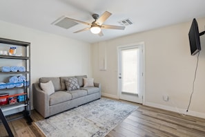 A living room with a grey sofa, a ceiling fan, a white door, and a TV mounted on the wall.