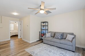 A living room with a grey sofa, a ceiling fan, and a bookshelf.