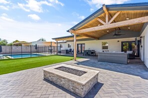 A covered patio area with a fire pit, outdoor furniture, and a swimming pool.