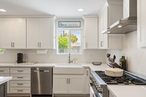 A modern kitchen with white cabinets, a stainless steel dishwasher, a gas stove, and a window with a view of trees.