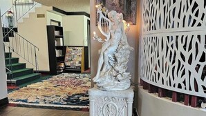 A statue of a woman playing a harp in a lobby with a staircase, bookshelves, and a patterned carpet. - Ocean  marina  hotel port alberni (Port Alberni)