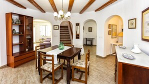 A dining area with a wooden table, chairs, and a cabinet with glass doors. - 055 Villa Retiro (Denia)