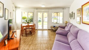 A living room with a wooden dining table, purple sofa, and a TV on a wooden stand. - 055 Villa Retiro (Denia)