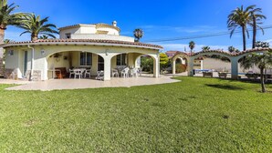 A house with a patio, outdoor seating, and palm trees. - 055 Villa Retiro (Denia)