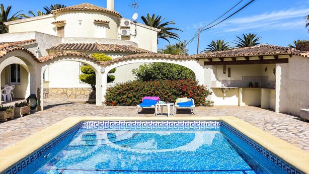 A pool area with a tiled pool, lounge chairs, and a building with arches and a tiled roof. - 055 Villa Retiro (Denia)