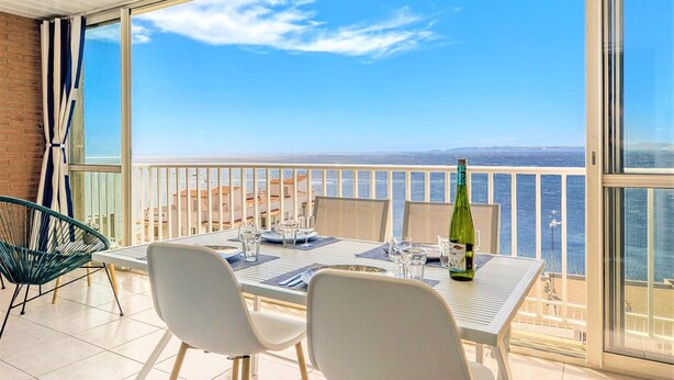 Un balcón con una mesa lista para dos personas, una botella de champán y vista al mar.