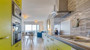 Una cocina moderna con armarios verdes, un ventanal grande y una zona de comedor con una silla azul.
