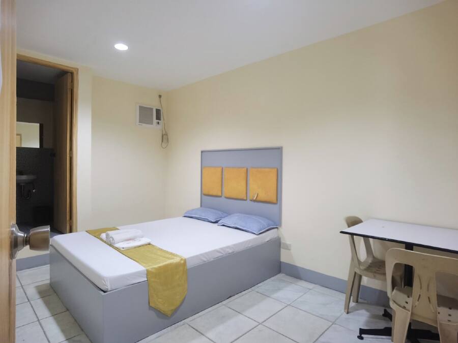 A single-bed room with a wooden door, a small desk, and a chair.