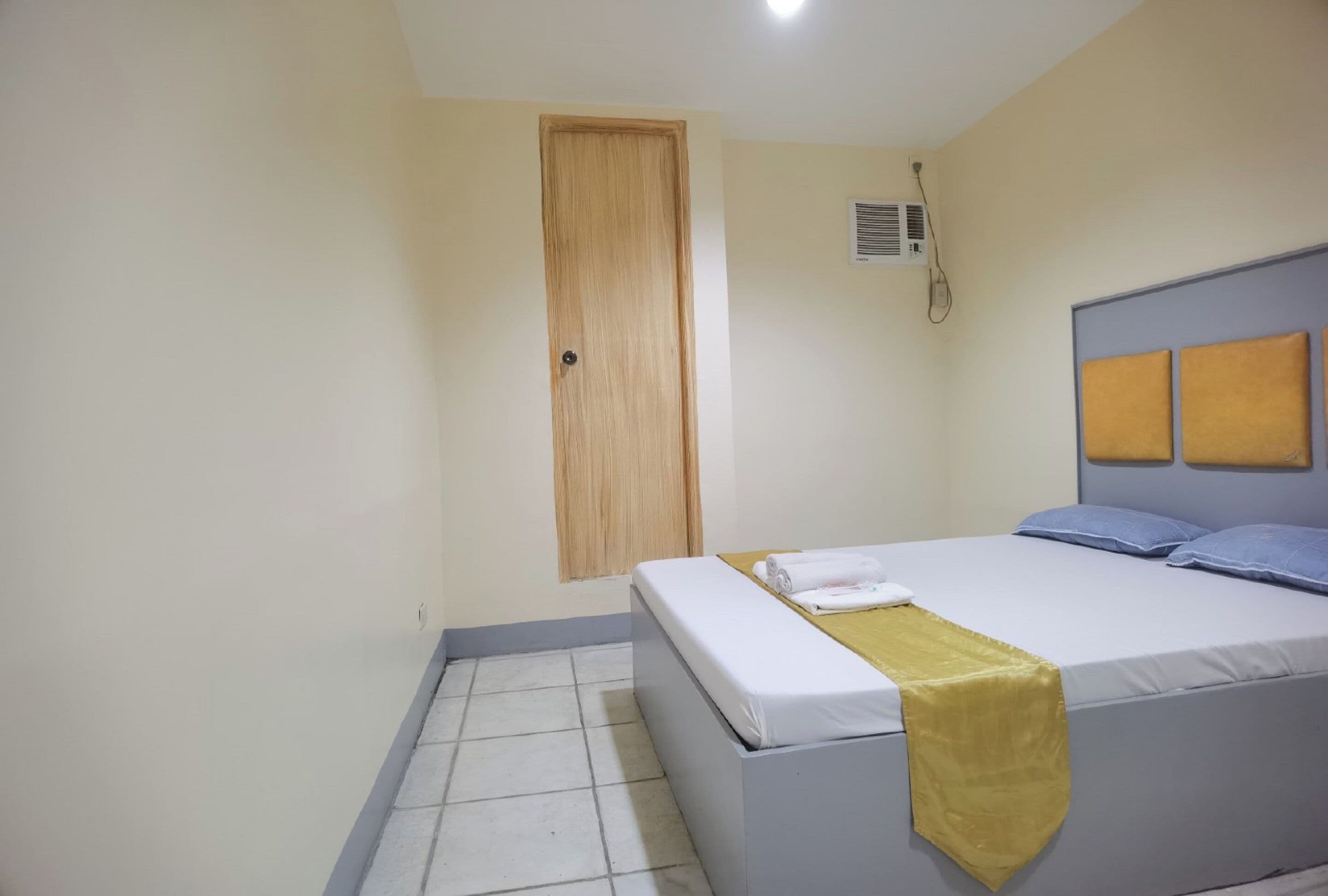 A bedroom with a bed, a wooden door, and a wall-mounted air conditioner.