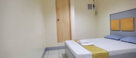 A bedroom with a bed, a wooden door, and a wall-mounted air conditioner.