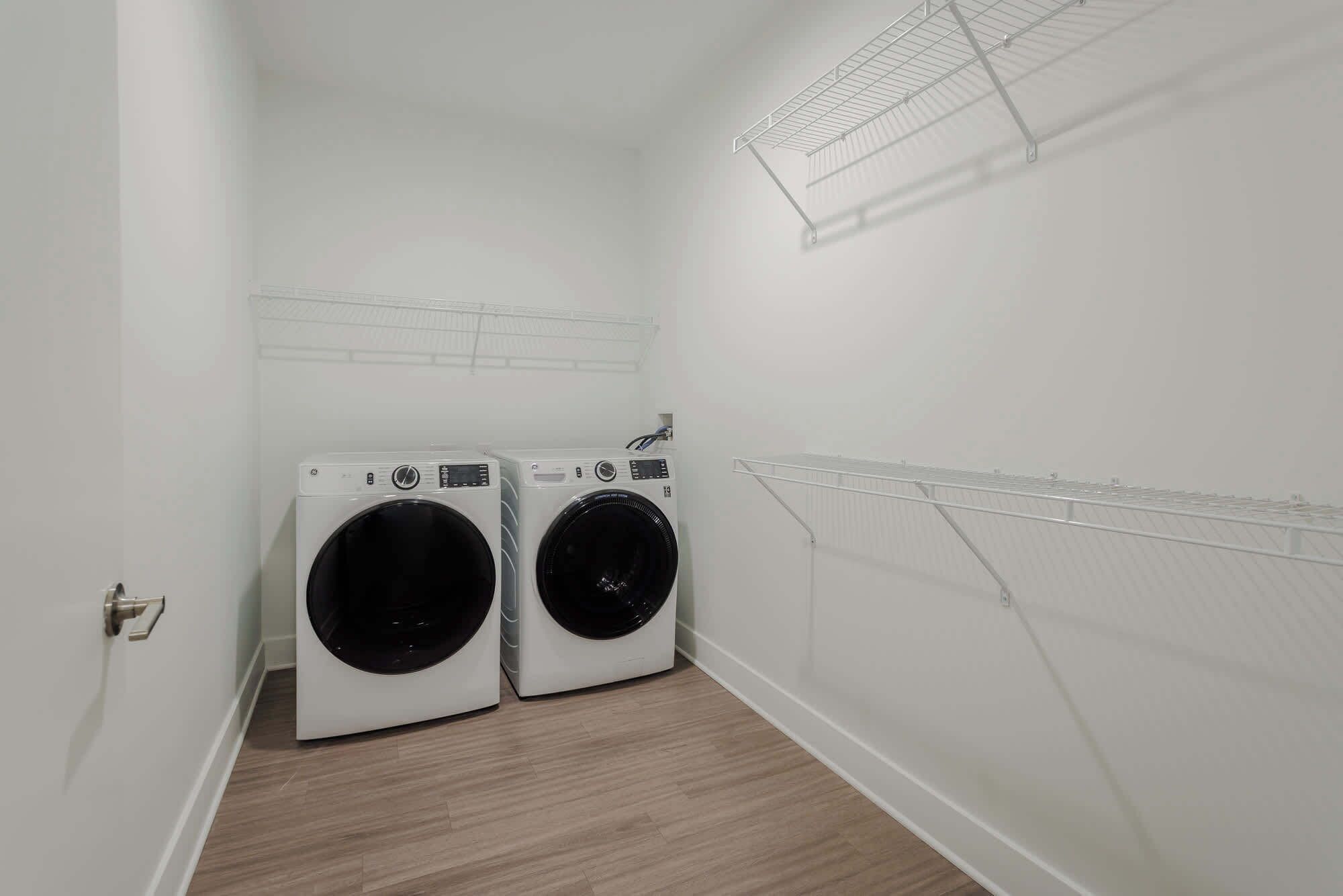 A laundry room with two front-loading washing machines, a metal drying rack, and a door with a handle.