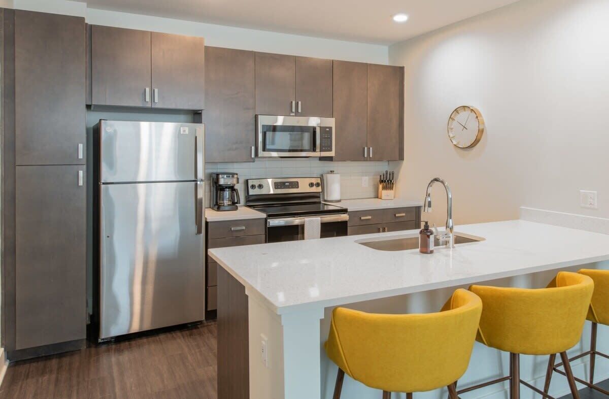 Una cocina moderna con electrodomésticos de acero inoxidable, una isla central con taburetes de bar y un reloj en la pared.