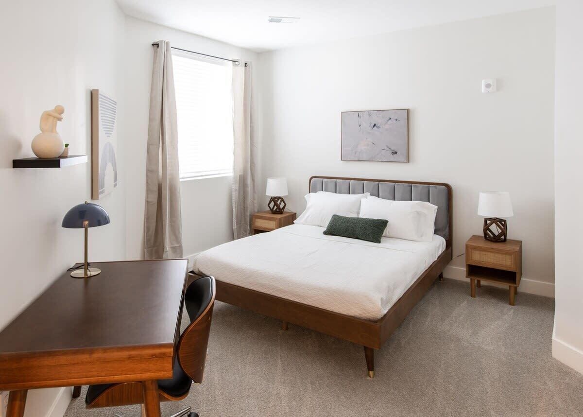 A neatly arranged bedroom with a bed, bedside tables, a desk, and a chair.