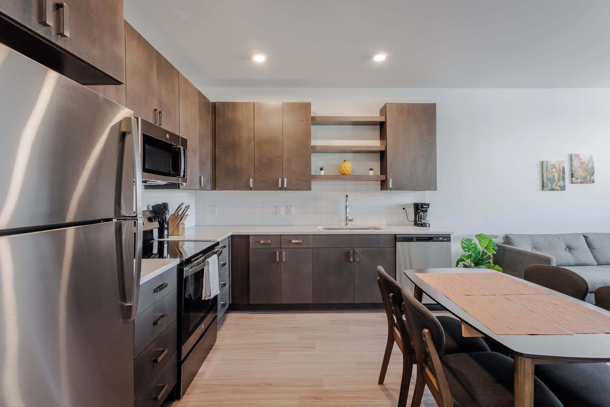 A modern kitchen with stainless steel appliances, dark wooden cabinets, and a wooden dining table.