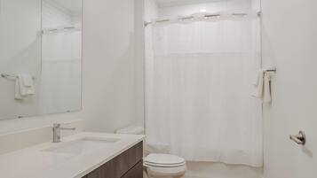 A modern bathroom with a large mirror, a sink, a toilet, and a shower curtain.