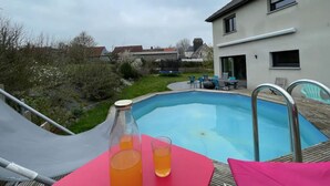 A swimming pool with a table and chairs, a bottle, and a glass of orange drink.