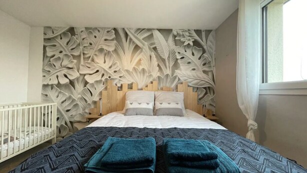 A bedroom with a large bed, a crib, and a wall with leaf patterns.