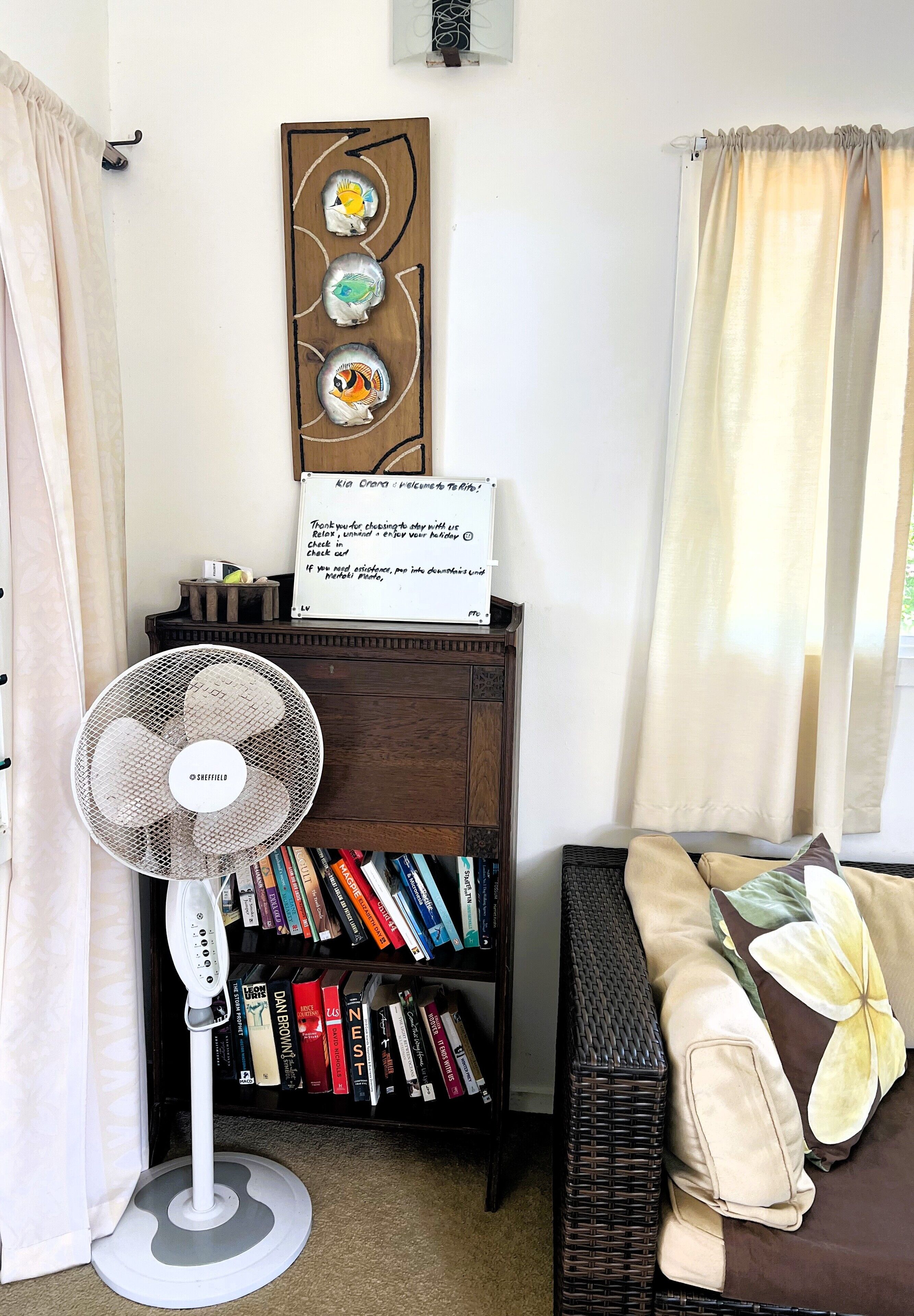 A cozy reading nook with a bookshelf, a fan, and a decorative sign.