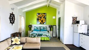 A compact hotel room with a bed, sofa, kitchenette, and a bright green accent wall. - Te Rito Lagoon Villas (Rarotonga)