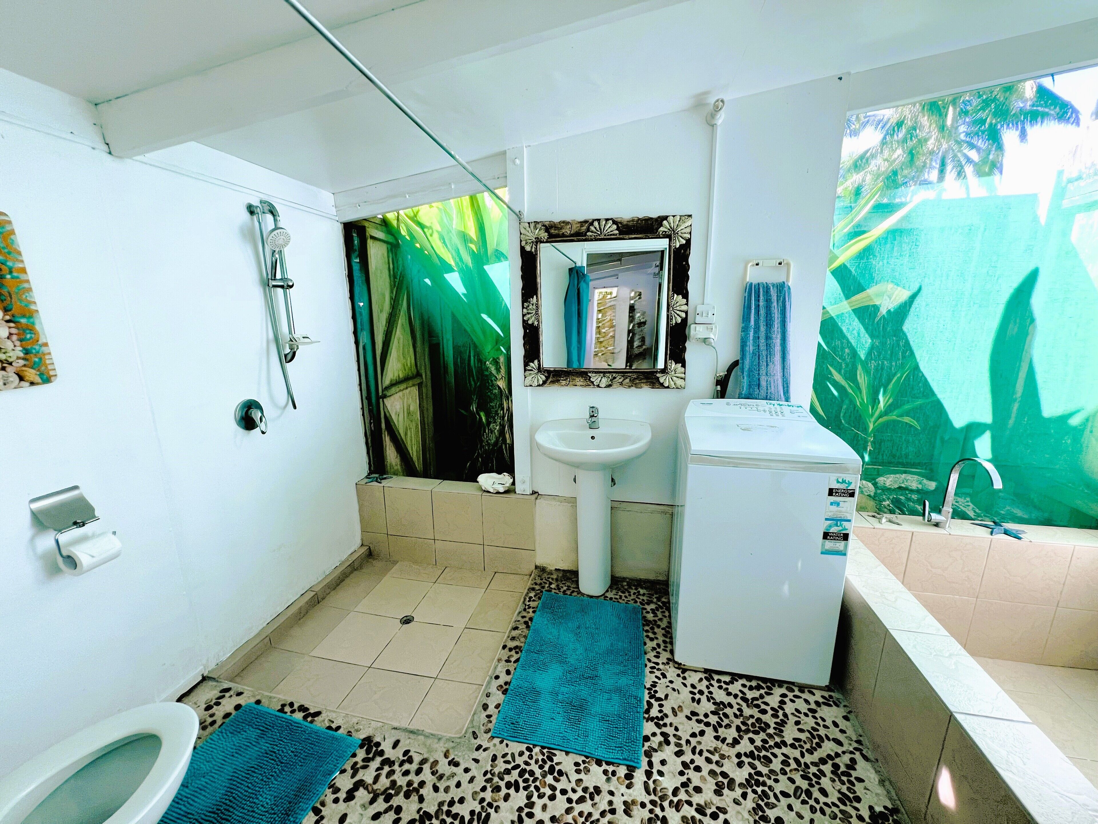 Une salle de bain équipée de toilettes, d’un lavabo, d’une douche et d’un miroir décoratif.