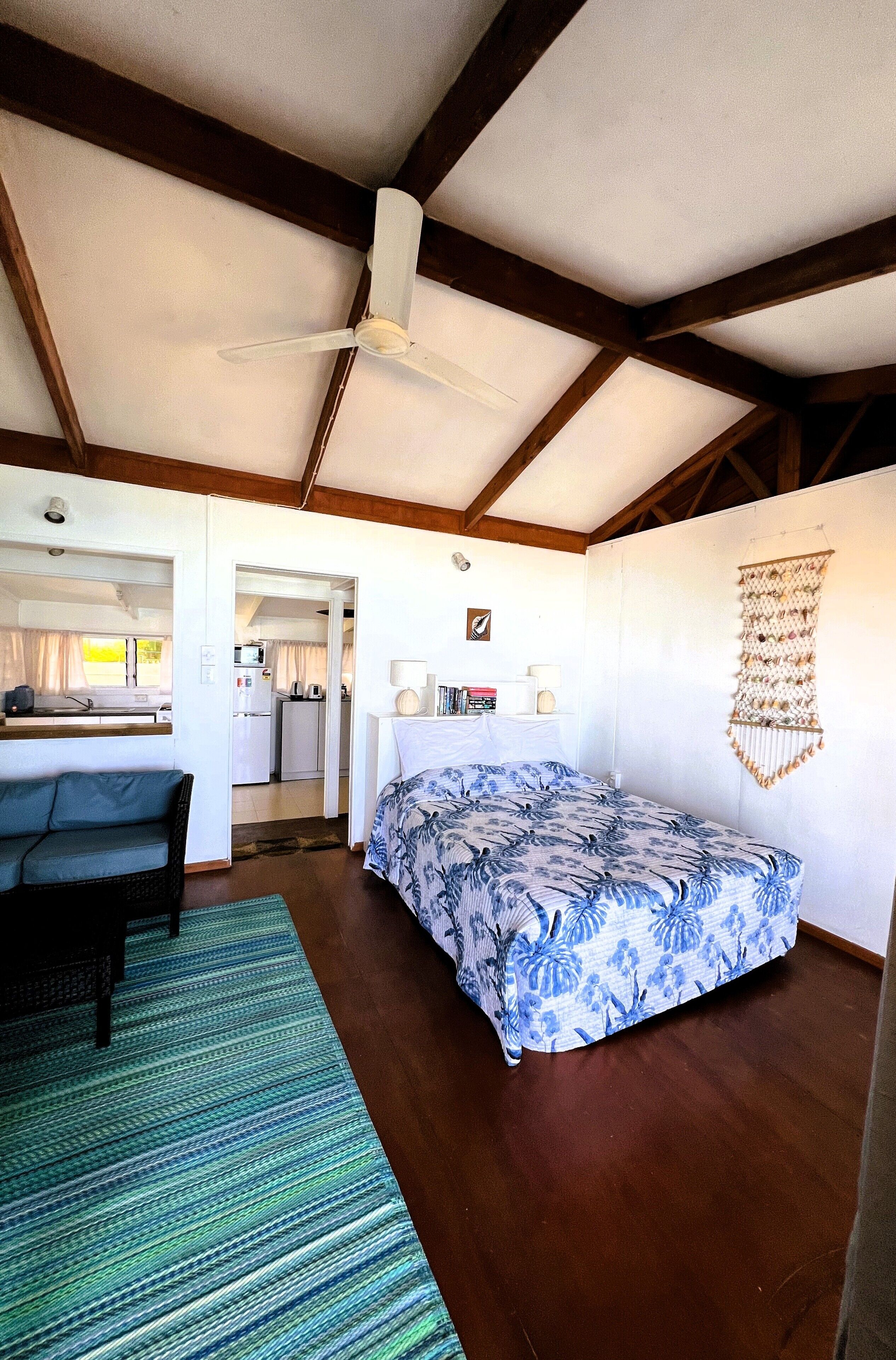 Ein Zimmer mit Bett, Sofa, Deckenventilator, Küchenzeile und Wanddekoration.
