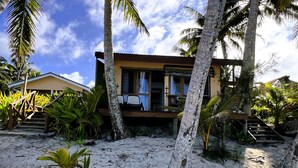 A beachfront property with a wooden staircase leading to a covered deck, surrounded by palm trees and tropical plants. - Te Rito Lagoon Villas (Rarotonga)