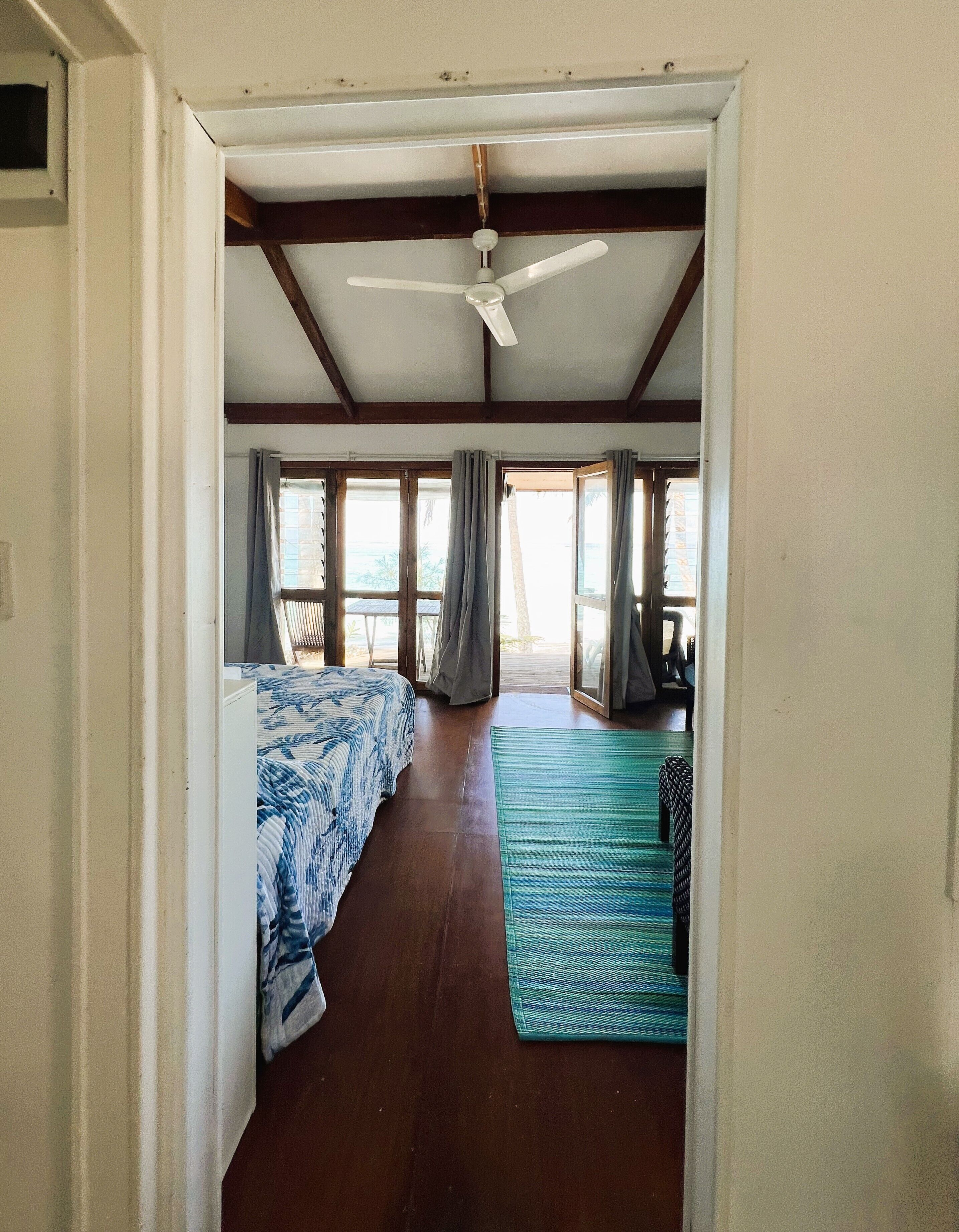A room with a bed, a ceiling fan, and a view of the outdoors.