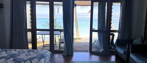 Une chambre avec un lit, un canapé et une vue sur la plage, visible à travers de grandes portes vitrées.