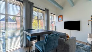 A modern living room with a dining table, grey sofa, and a flat-screen TV mounted on the wall. - Cozy apartment in the heart of Sneek (Friesland)