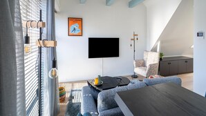 A modern living room with a flat-screen TV mounted on the wall, a sofa, a coffee table, and a dining table. - Cozy apartment in the heart of Sneek (Friesland)