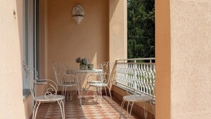 A balcony with a checkered floor, white metal chairs, a small round table, and a vase with flowers.