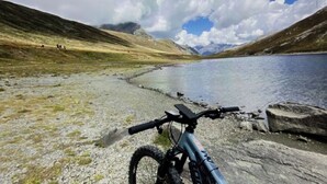 A mountain bike parked on a rocky shore with a lake and mountains in the background.