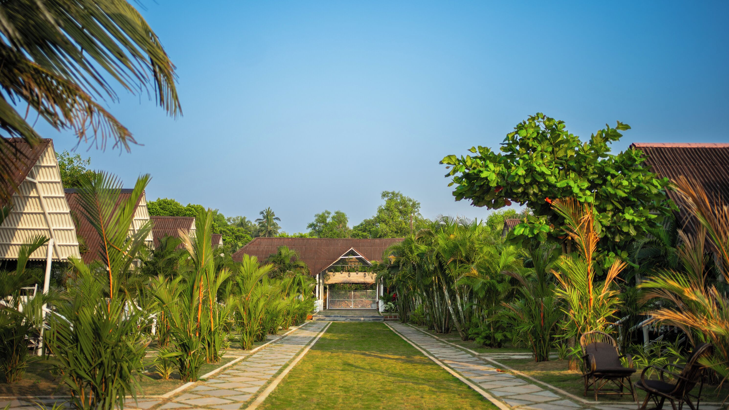 A pathway leading to a building with a traditional roof, surrounded by lush greenery and palm trees.