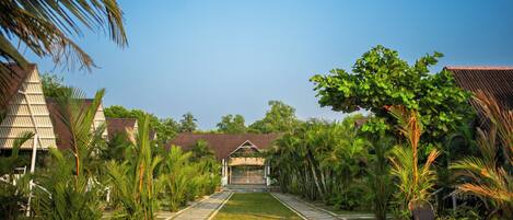 A pathway leading to a building with a traditional roof, surrounded by lush greenery and palm trees.