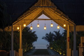 A covered walkway with hanging lights leading to a beach. - Royal Agonda (Canacona)