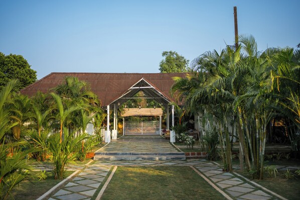 A covered outdoor area with a tiled pathway leading to a gated entrance, surrounded by palm trees and greenery. - Royal Agonda (Canacona)