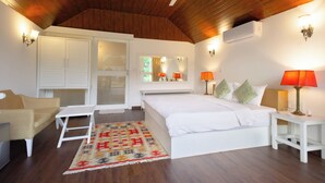 Quarto com teto de madeira, cama branca, duas mesas de cabeceira com luminárias, uma mesinha branca e um tapete colorido.