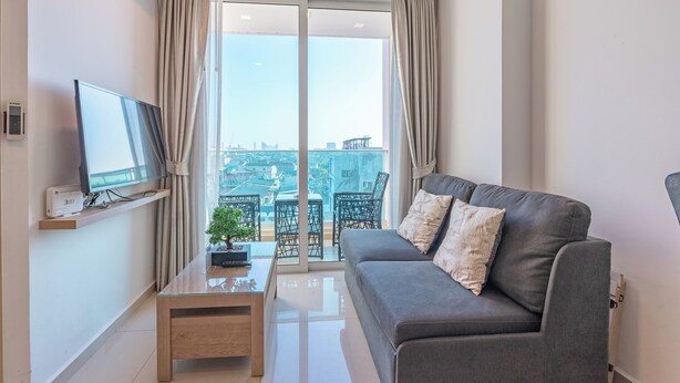 A modern living room with a grey sofa, a TV on a shelf, a small table, and a balcony with a view of the city. - City Garden Tower by Pattaya Holiday (Pattaya)
