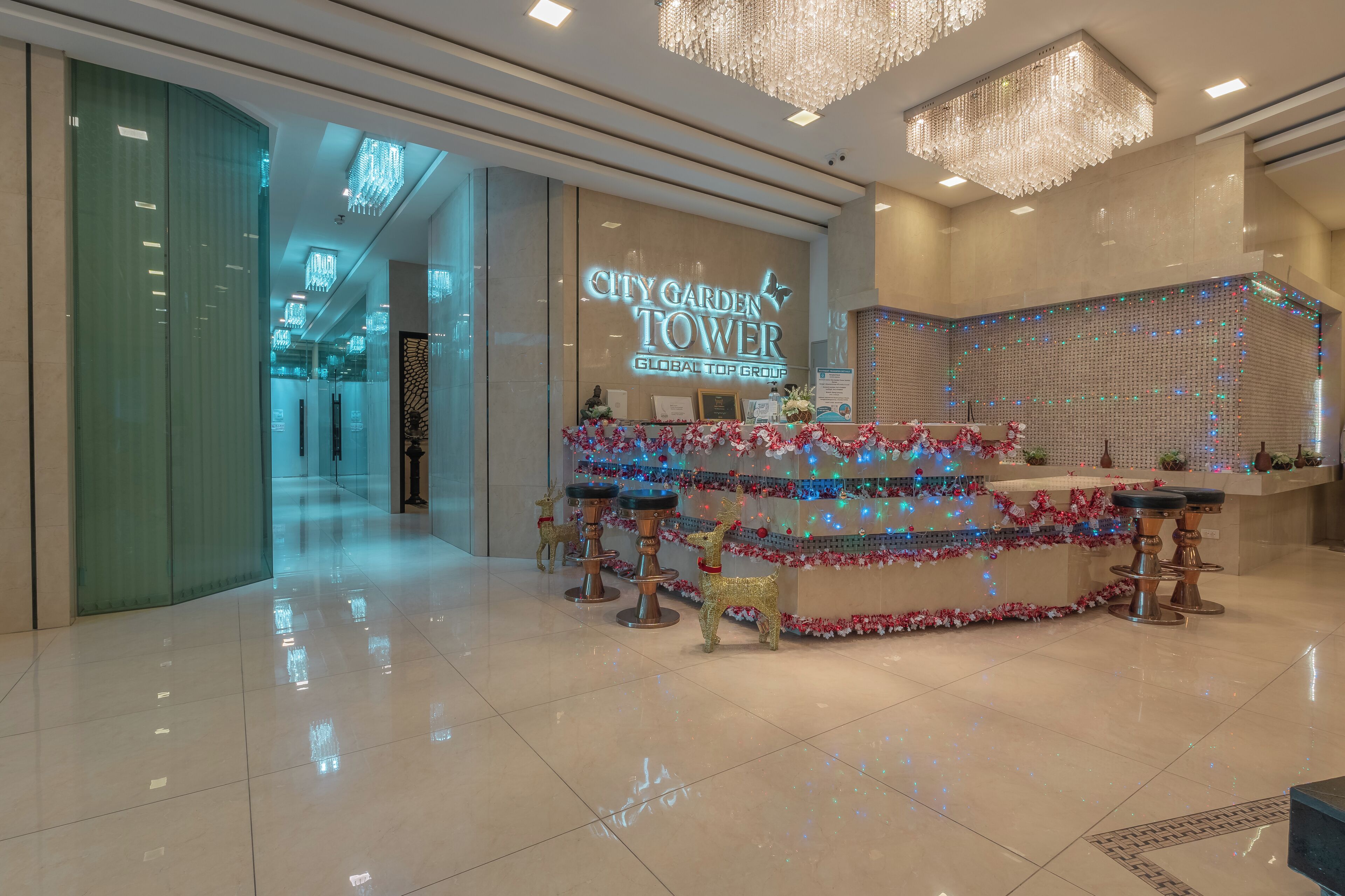 A hotel lobby with a reception desk decorated with festive lights and reindeer statues.
