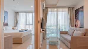 A modern hotel room with a bed, a sofa, a glass table, and a balcony with curtains. - City Garden Tower by Pattaya Holiday (Pattaya)