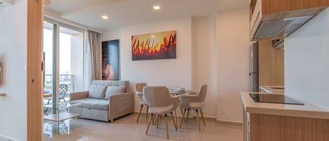 A modern living room with a sofa, dining table, and chairs, a kitchen area with a countertop, and a large window with curtains.