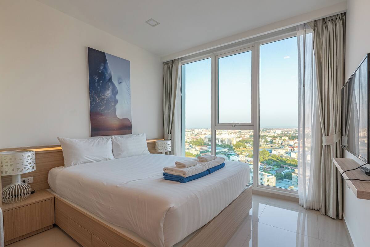 Ein modernes Hotelzimmer mit einem großen Bett, Blick auf die Stadt und einem Gemälde an der Wand.