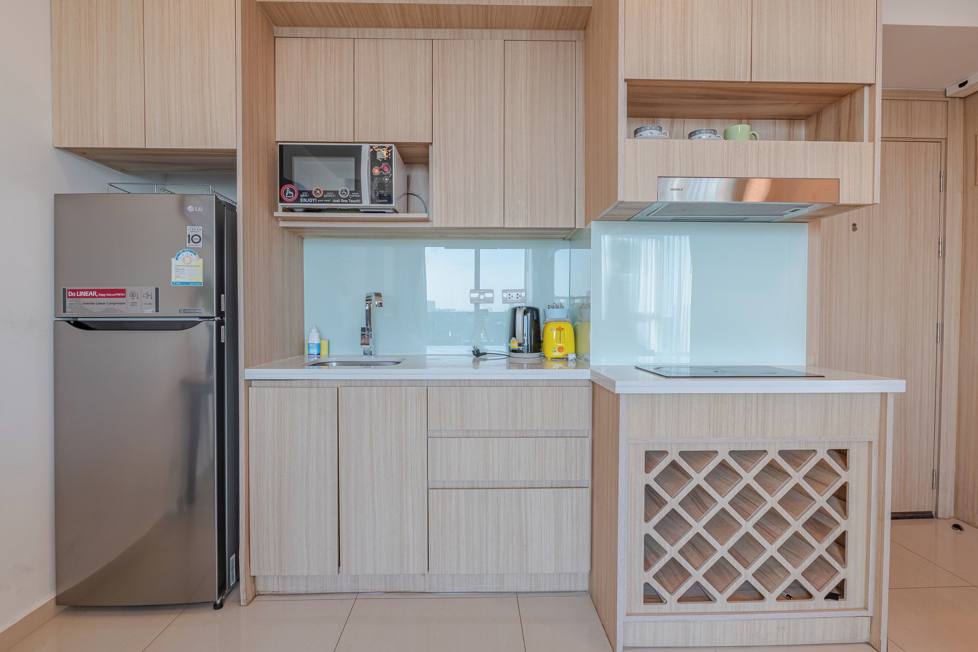 Eine moderne Küche mit hellen Holzschränken, einem Edelstahlkühlschrank, einer Mikrowelle und einem Einbauofen.