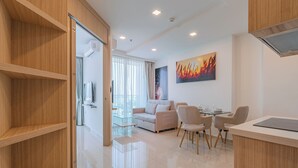 A modern living room with a sofa, chairs, a glass coffee table, and a dining area with a table and chairs. There is a large window with curtains, a painting on the wall, and a wooden cabinet. - City Garden Tower by Pattaya Holiday (Pattaya)